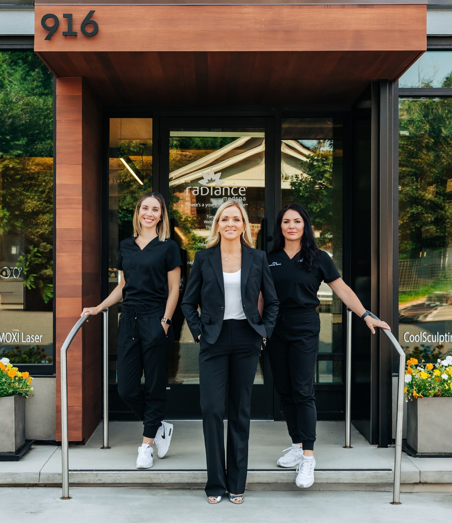 Three staff members stand on the spa storefront steps, smiling at the camera in black uniforms.