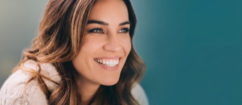 Close-up of a smiling woman with brown hair in a knit sweater, looking off to the side.