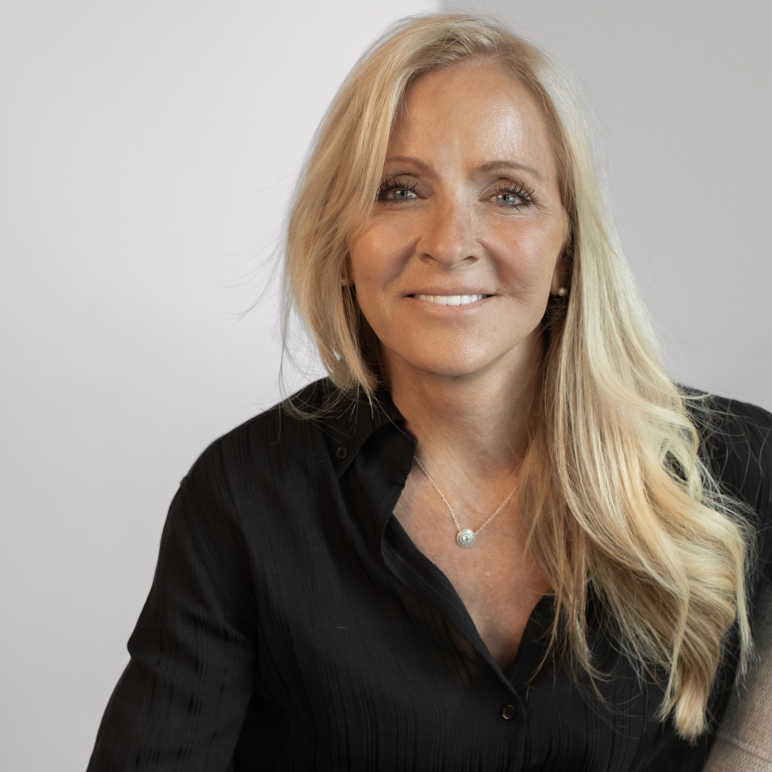 Portrait of a smiling blonde woman in a black button-down shirt, facing the camera